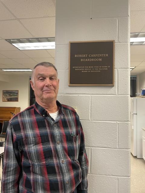 Robert Carpenter standing in front of the dedication plaque for the Robert Carpenter Boardroom.